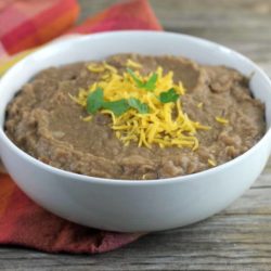 Refried beans topped with cheese and cilantro in a white bowl.