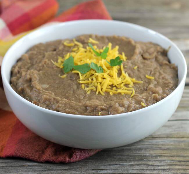 Refried beans topped with cheese and cilantro in a white bowl.