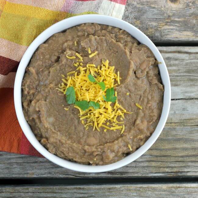 Refried beans topped with cheese and cilantro in a white bowl.