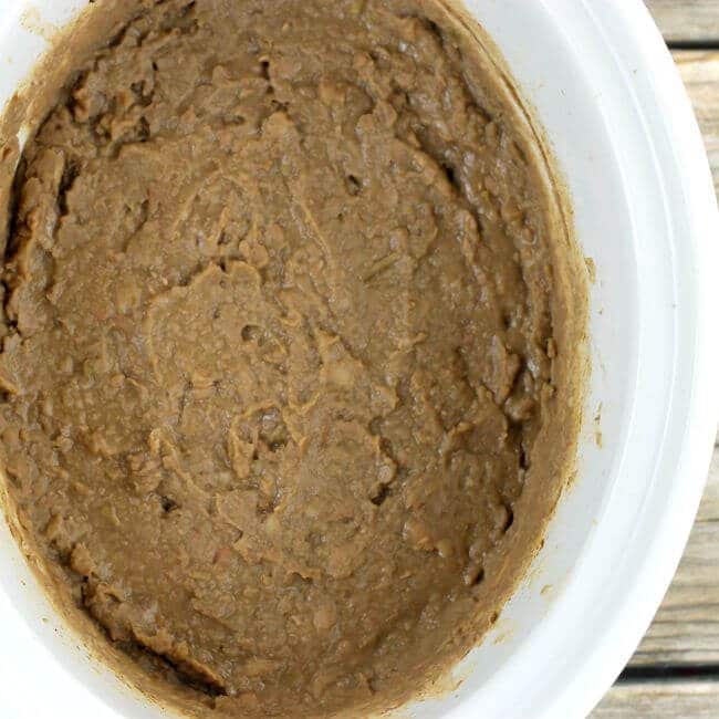 Mashed refried beans in a white slow cooker.