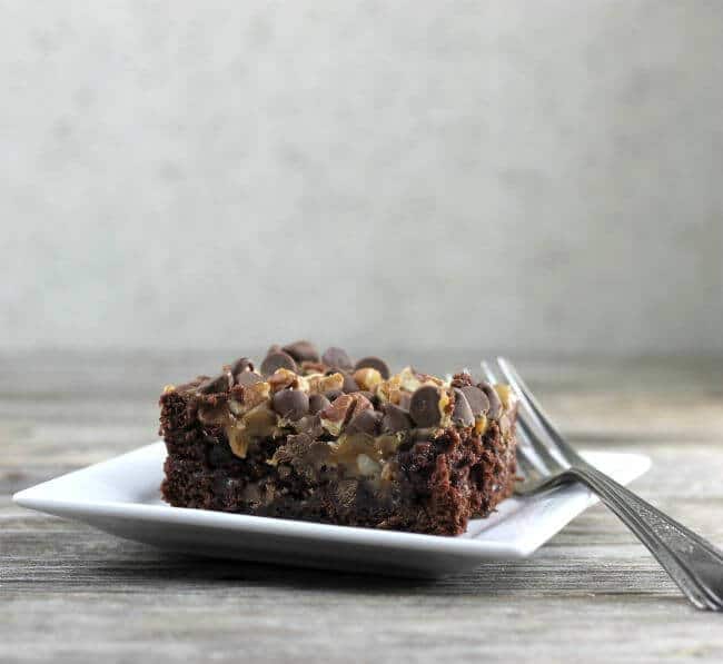 Side view of turtle dump cake on a white plate with a fork.