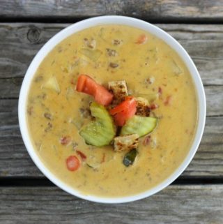 Cheeseburger soup with pickles and tomatoes for a topping in a white bowl.
