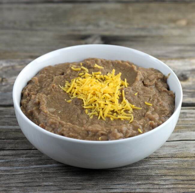 Refried beans topped with cheddar cheese in a white bowl.