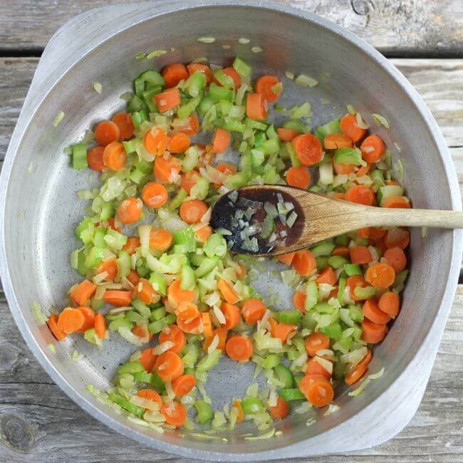 Cooked vegetables in a Dutch oven with a spoon for stirring.