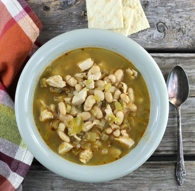 White chicken chili in a bowl with a napkin, spoon, and crackers on the side.