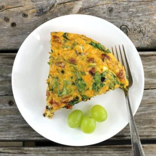 A slice of a chorizo frittata with a green grapes and a fork on a white plate.