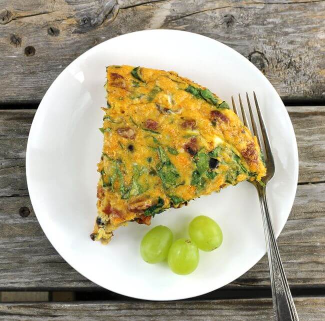 A slice of a chorizo frittata with a green grapes and a fork on a white plate.