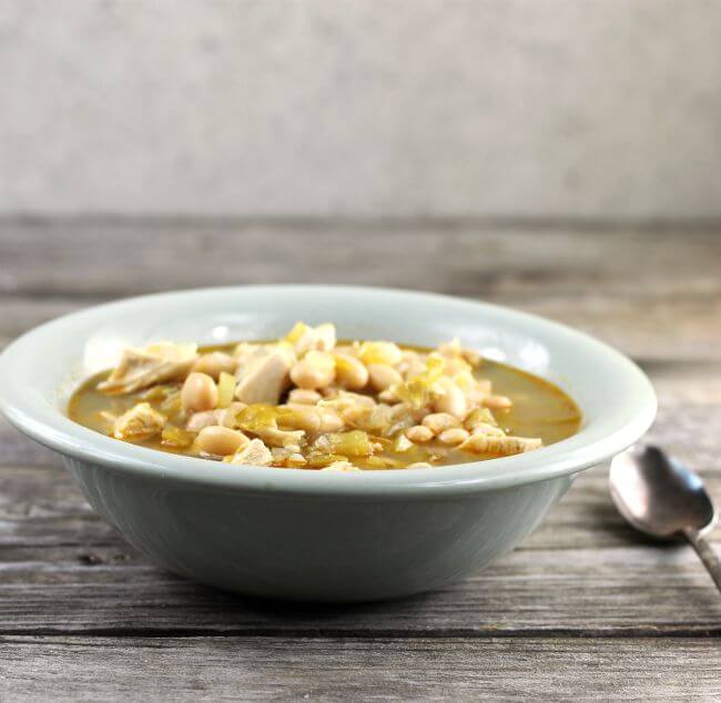 White chicken chili in a green bowl with sppon by the side of the bowl.