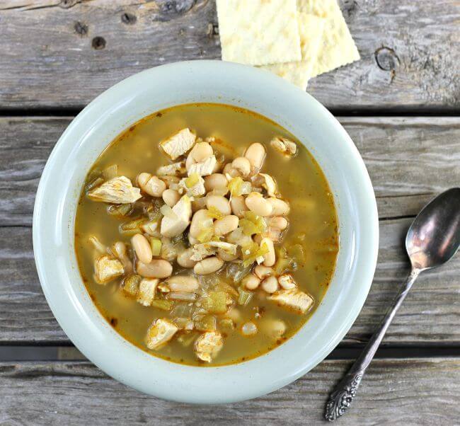 White chicken chili in a green bowl with crackers and spoon on the side.