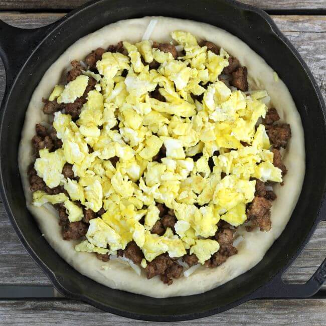 Sausage breakfast pizza with breakfast sausage and egg spread over the pizza dough in the skillet.