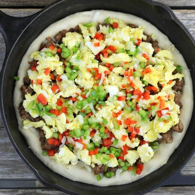 Sausage breakfast pizza with breakfast sausage, scrambled eggs, and veggies spread over top of the pizza dough in the skillet.