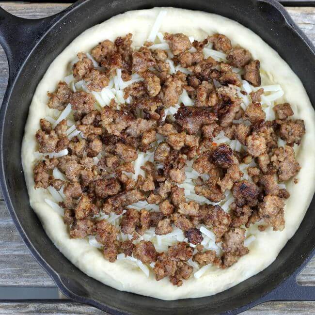 Sausage breakfast pizza with breakfast sausage spread over top of the crust in the skillet.