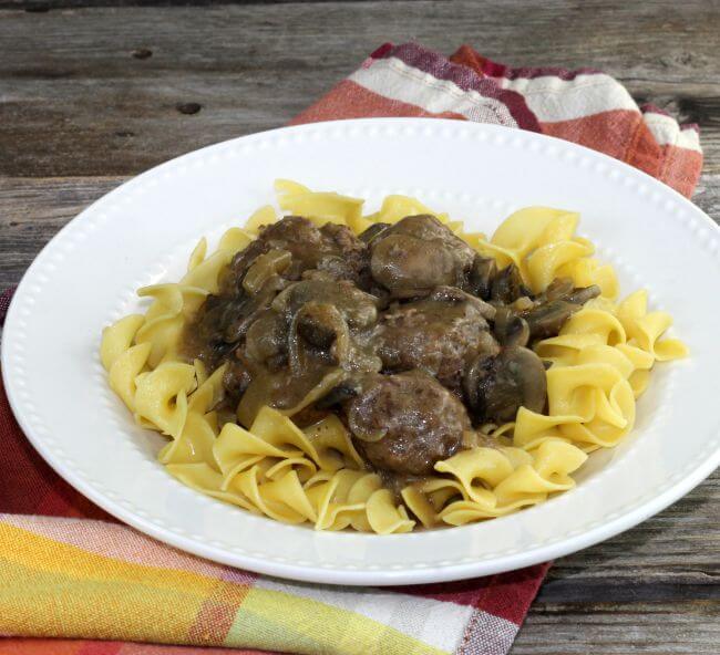 Meatballs and egg noodles in a white bowl setting on a napkin.