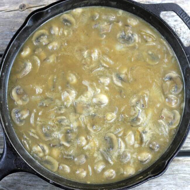 Gravy with onion and mushrooms in a skillet.