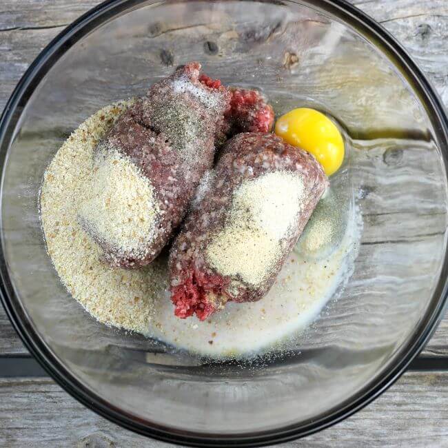 Hamburger, bread crumbs, egg, and milk in a glass bowl.