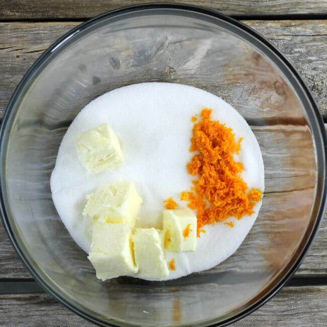 Sugar, butter, and orange zest in a glass bowl.