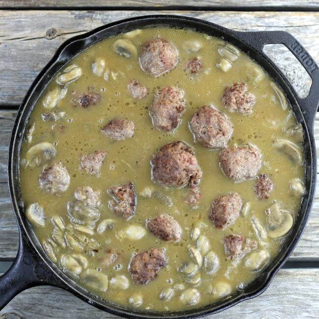 Meatballs in a onion and mushroom gravy in a skillet.