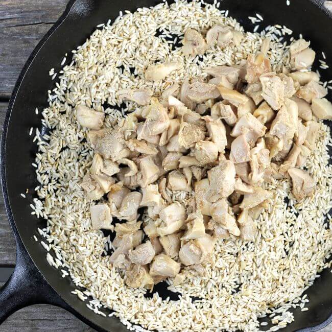 Adding chicken to the skillet with the fried rice.