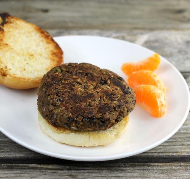 Side angle view of a veggie burger on a bun set on a white plate.