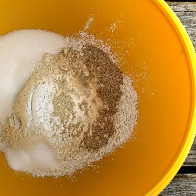 Flour, sugar, yeast, and salt in a orange bowl.