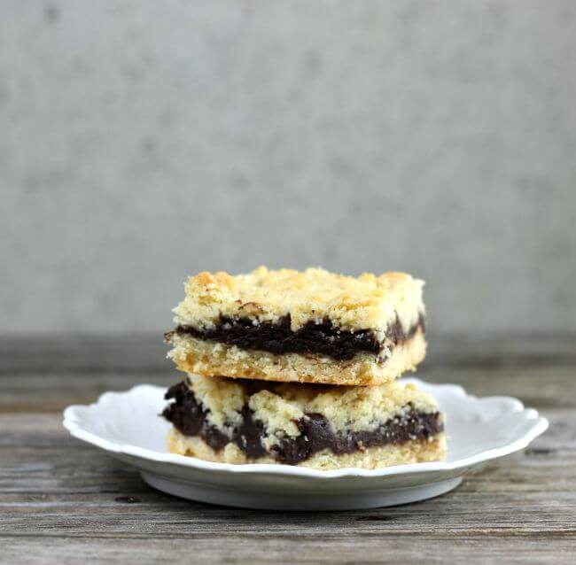 Side view of two chocolate layer bars on a white plate.