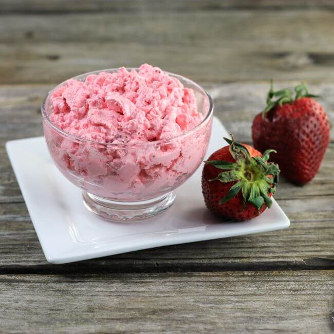 Side angle view of the jello salad in a glass bowl set on a white plate with strawberries.