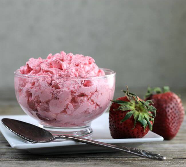 Side view of a jello salad in a glass bowl setting on a white plate with strawberries.