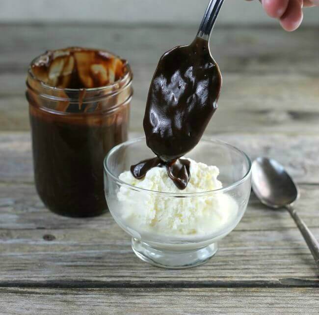 A spoon adding chocolate to a bowl of ice cream.