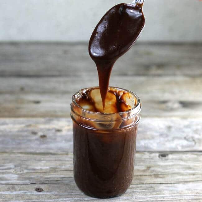 A spoon scooping out chocolate sauce from a jar.
