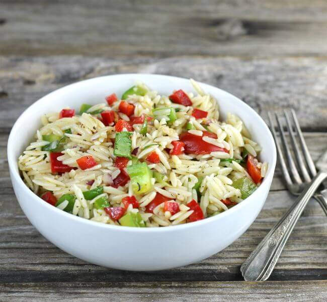 Side angle view of orzo pasta salad in a white bowl.