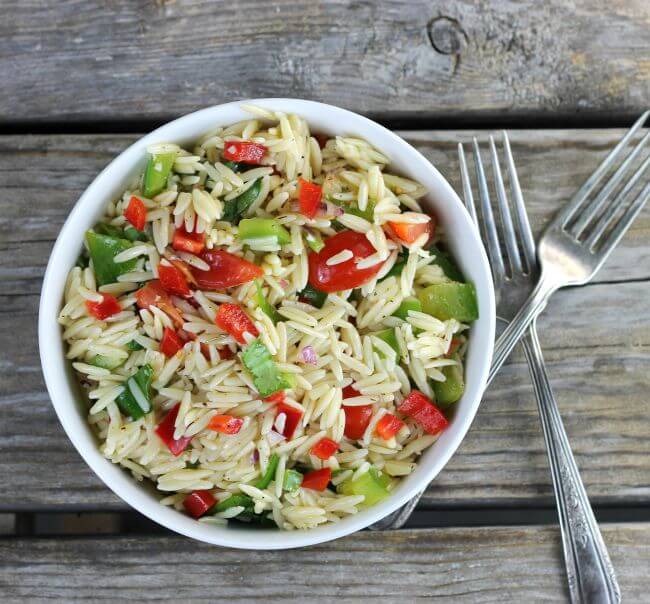 Orzo salad in a white bowl with forks on the side.