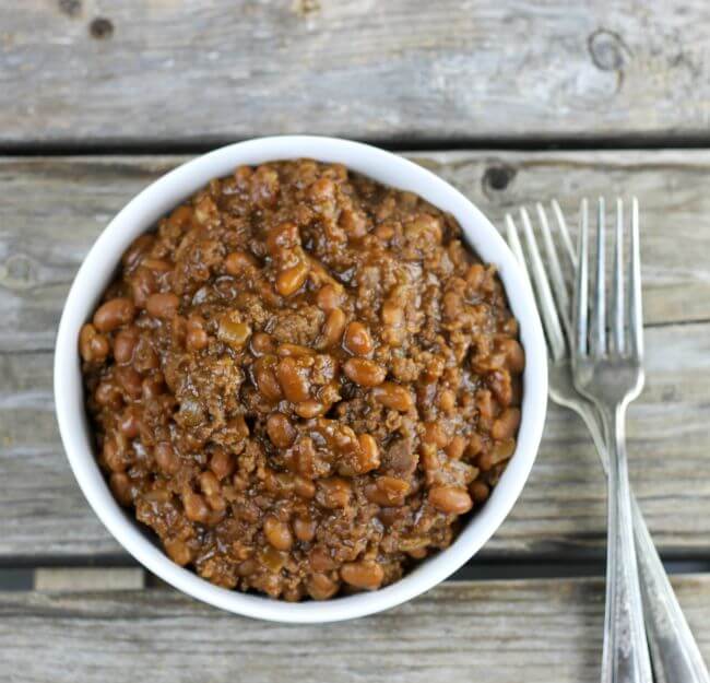 Looking down at a white bowl with baked beans with two forks on the side.