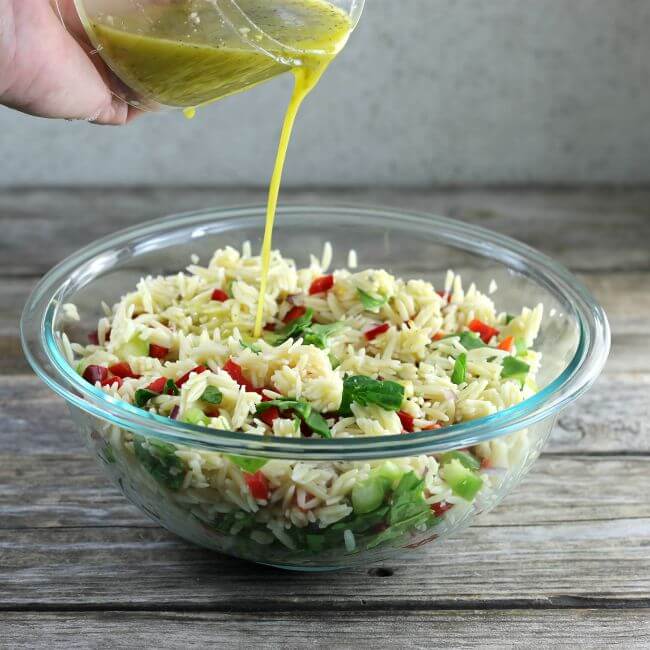 Pouring dressing on the orzo salad.