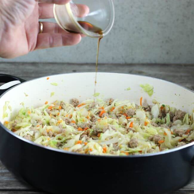 Soy sauce is added to the pork and cabbage in the skillet.