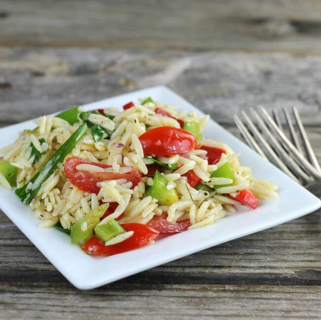 Side angle view of orzo salad on a square white plate.