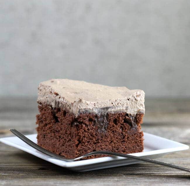 Chcolate poke cake on a white plate with a fork.