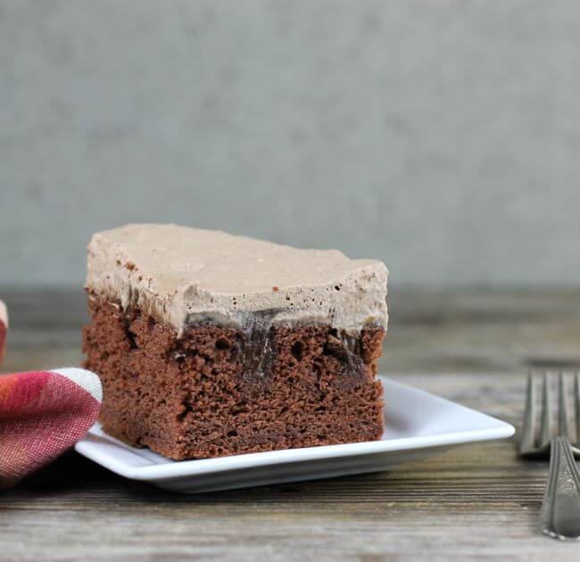 Side view of chocolate poke cake on a white plate with a napkin and for on the sides of the plate.