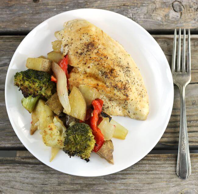 Looking down at a plate that has a chicken breast and vegetables with a fork on the side.