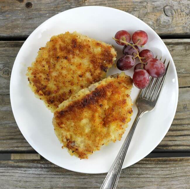 Looking down at two pork chops on a white plate with grapes and a fork.