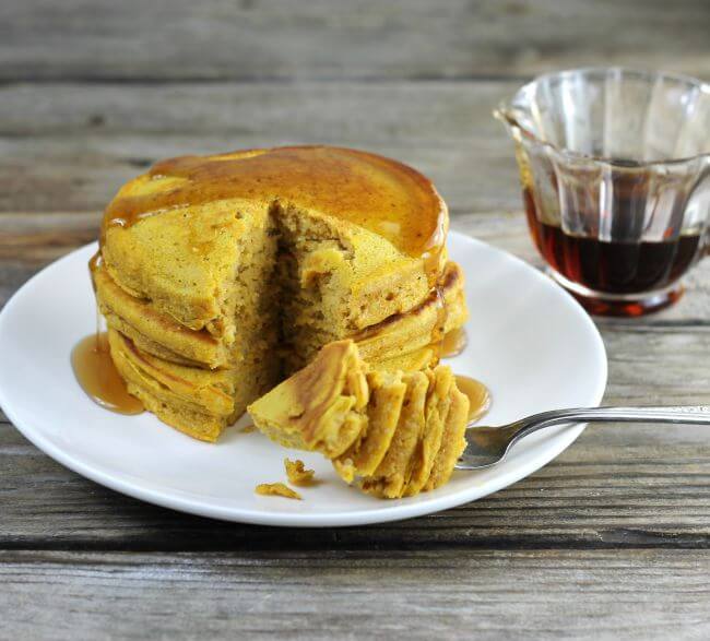 Side angle view of pancakes with a container of syrup behind the plate.