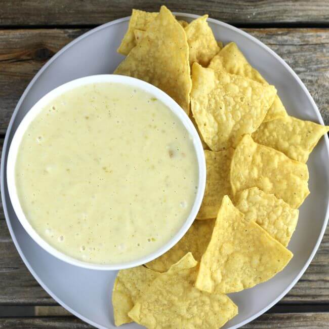 Looking down at a bowl of questo on a plate with tortilla chips.