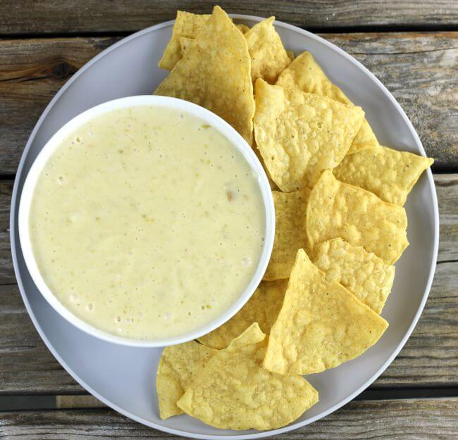 Over looking a plate with a bowl of queso with a side of chips.