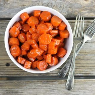 Overview of a bowl of glazed carrots with two forks on the side.