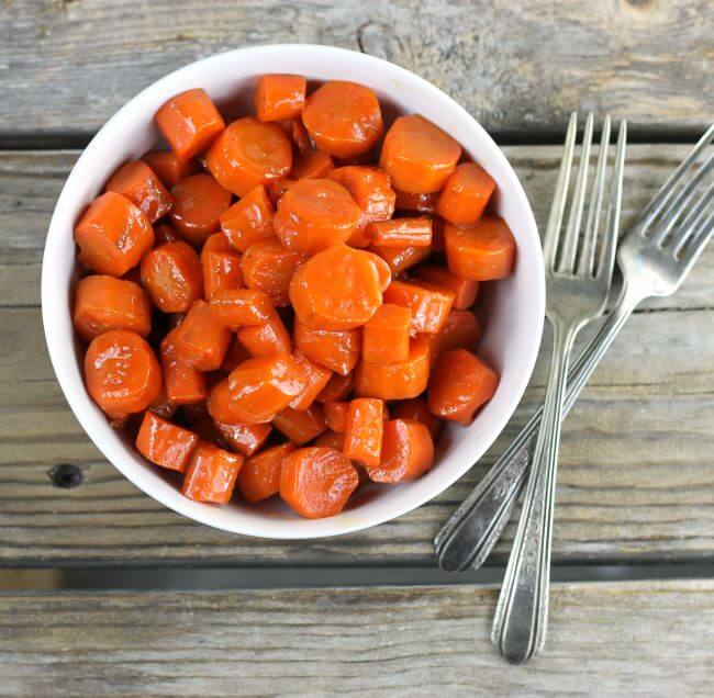 Overview of a bowl of glazed carrots with two forks on the side.