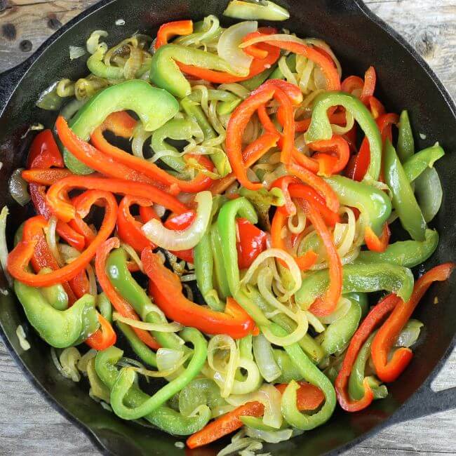 Geen peppers, red peppers, and onions in a skillet.