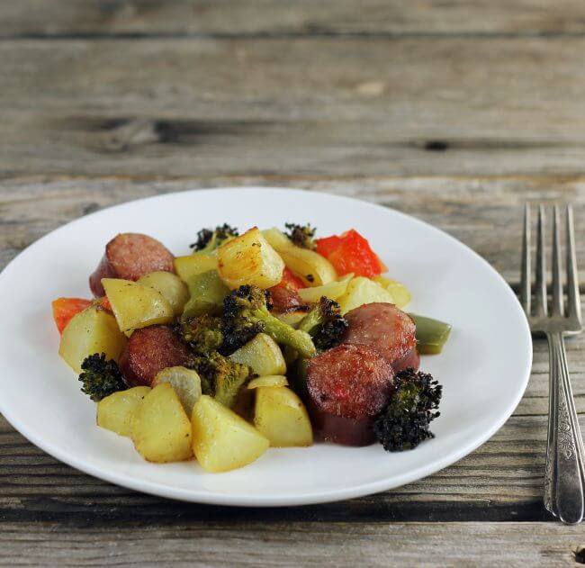 A side angle view of a plate of roasted vegetable with sausage.