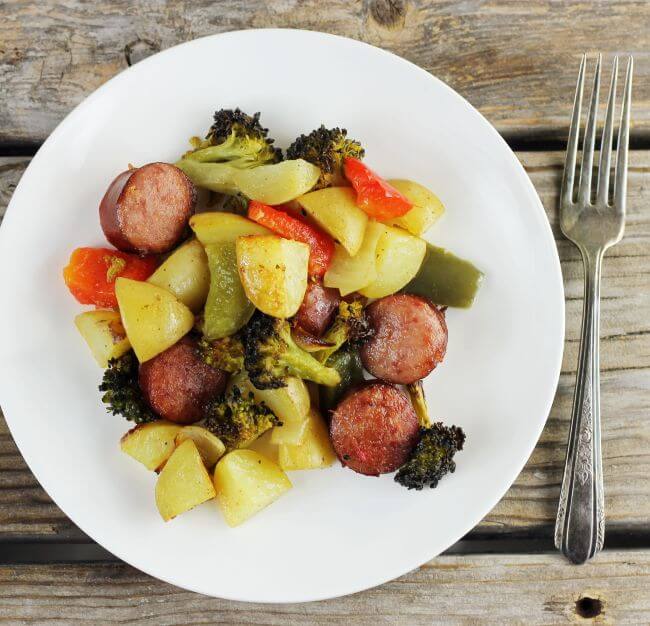 Looking down at a white plate with roasted sausage and vegetables.