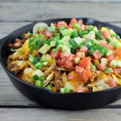 A side view of chicken nachos in a cast-iron skillet.