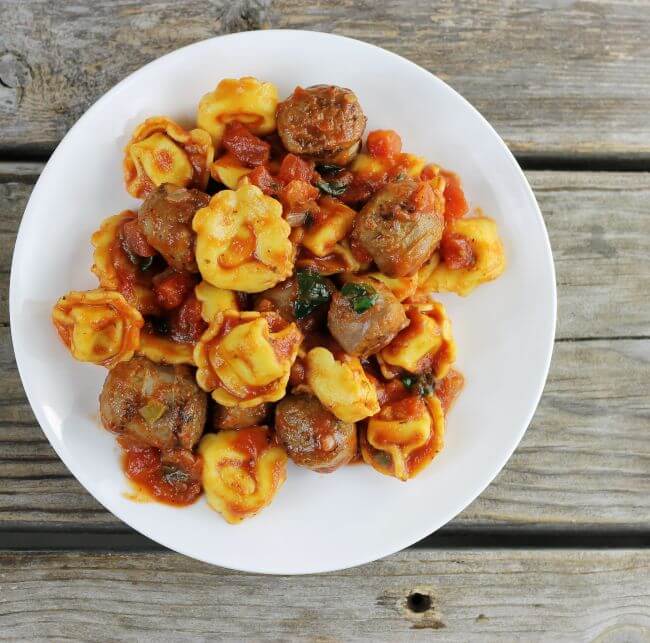 Over looking a plate loaded with Italian sausage and tortellini.