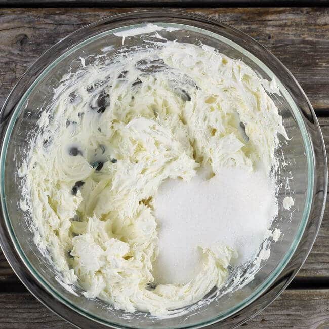 Sugar is added to the cream cheese in the bowl.